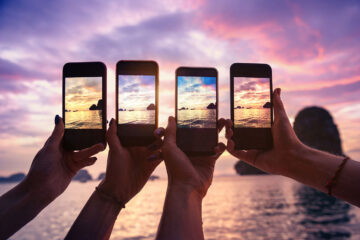 four hands with mobile phones taking photo of the sky